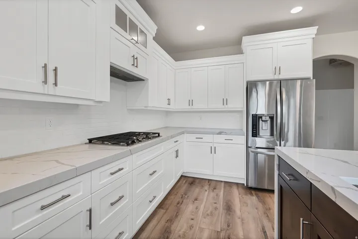 Modern kitchen featuring white shaker cabinetry, light-toned countertops with subtle veining, a tile backsplash, stainless steel appliances, and wood-finish flooring