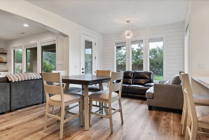 Open-concept living space featuring wood-finish flooring, white shiplap accent wall, large windows, and a contemporary chandelier