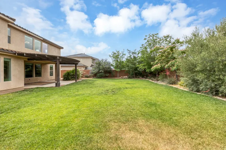 Expansive backyard featuring a lush lawn, mature perimeter landscaping, and a covered patio area with a wooden pergola