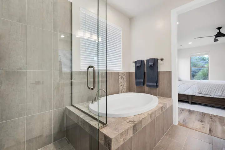 Tiled bathroom featuring a built-in soaking tub, a glass-enclosed shower, a rectangular window with blinds, and recessed lighting