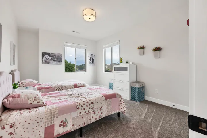 Bedroom featuring a neutral wall color, two windows, and dark textured carpeting
