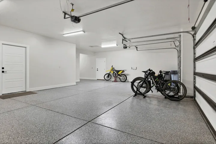 Spacious garage featuring a durable epoxy floor coating, multiple overhead fluorescent light fixtures, an automatic garage door opener, and two white interior doors