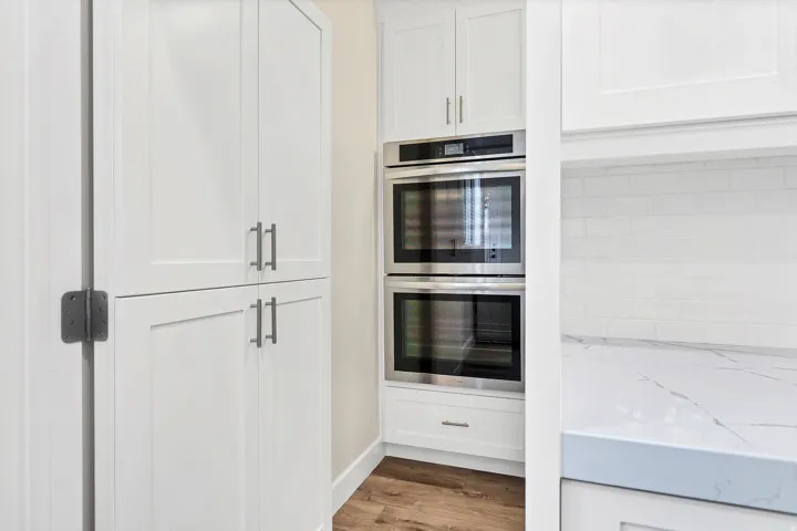 White shaker cabinetry featuring brushed nickel hardware, stainless steel double ovens, and wood-finish flooring