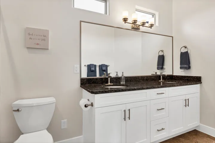 Double vanity featuring white cabinetry, dark countertop, and brushed nickel hardware