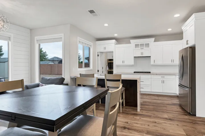 Open-concept kitchen and dining area featuring wood-finish flooring, white shaker cabinetry, stainless steel appliances, and a central island with bar seating