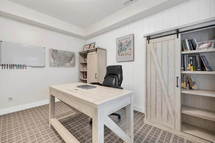 Dedicated workspace featuring a patterned carpet, white shiplap accent wall, and a large light wood-finish desk