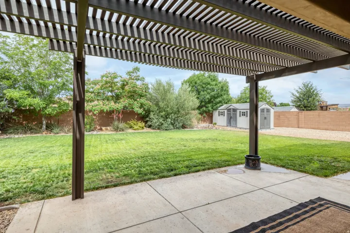 Expansive backyard featuring a shaded patio with a slatted pergola, a manicured lawn, and two detached storage sheds