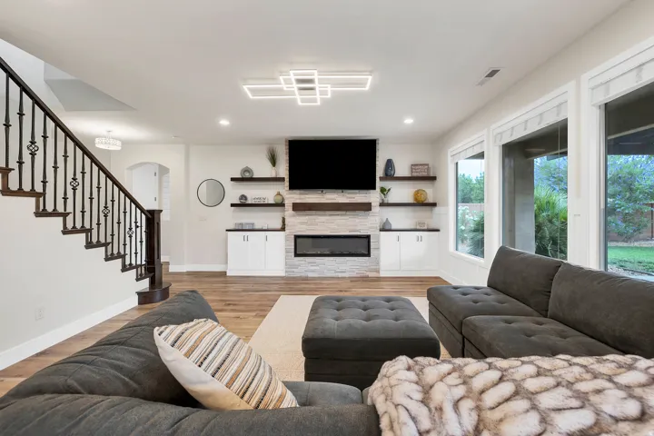 Spacious living area featuring wood-finish flooring, a contemporary linear fireplace with stone surround, and an integrated media wall with floating shelving and built-in cabinetry
