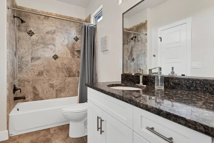 Bathroom featuring a white bathtub, tiled shower surround with decorative accents, a built-in shower niche, and a single vanity with a dark countertop and undermount sink