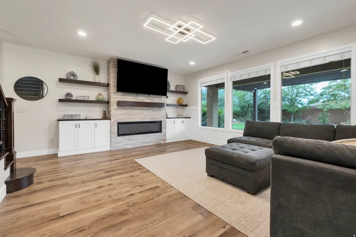 Living area featuring wood-finish flooring, a contemporary linear electric fireplace with stone surround, custom built-in cabinetry, and integrated shelving