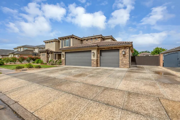 Mediterranean-style residence featuring a tile roof, stucco and stone facade, dual garage doors, and an expansive concrete driveway