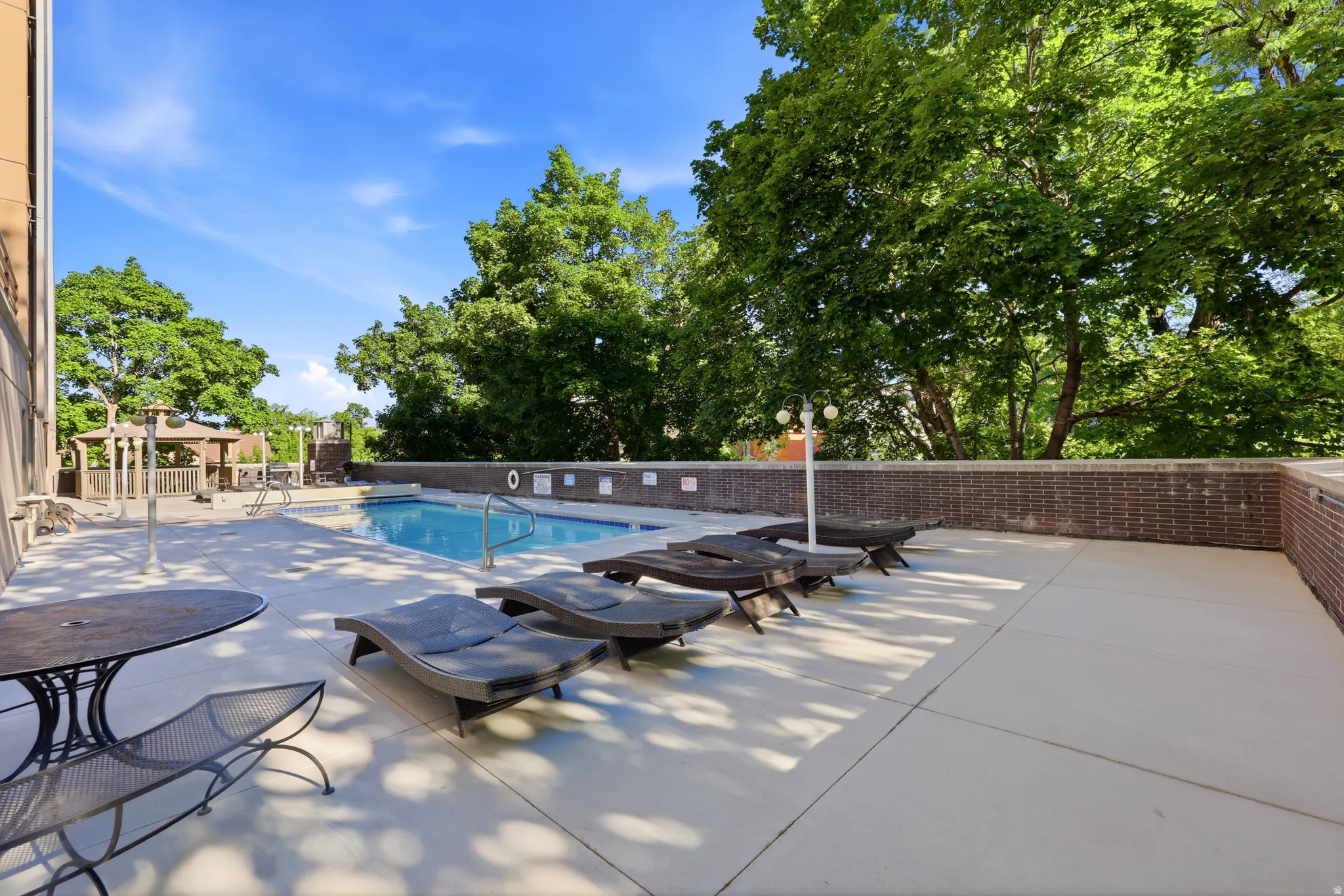 Outdoor pool area featuring a perimeter brick wall, concrete decking, and mature trees providing natural shading