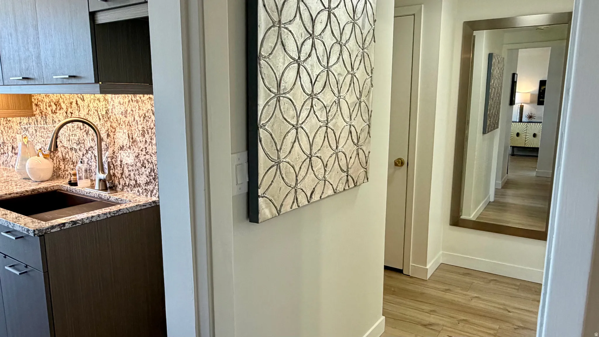 Modern kitchen area featuring dark wood-finish cabinetry, a stone countertop, a mosaic tile backsplash, and an undermount sink with a gooseneck faucet