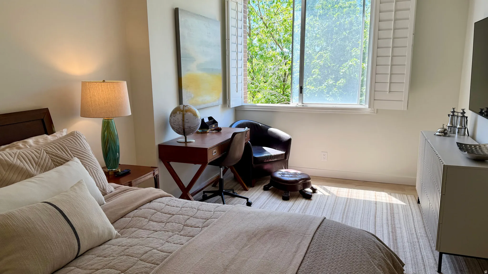 Inviting bedroom featuring ample natural light, a built-in window, plantation shutters, light wood-finish flooring, and a dedicated desk area