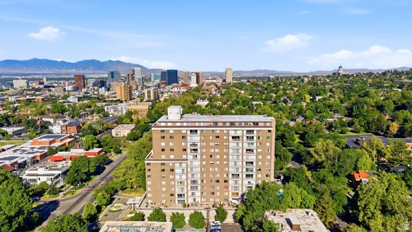 High-rise property featuring a brick exterior and multiple balconies, surrounded by mature trees