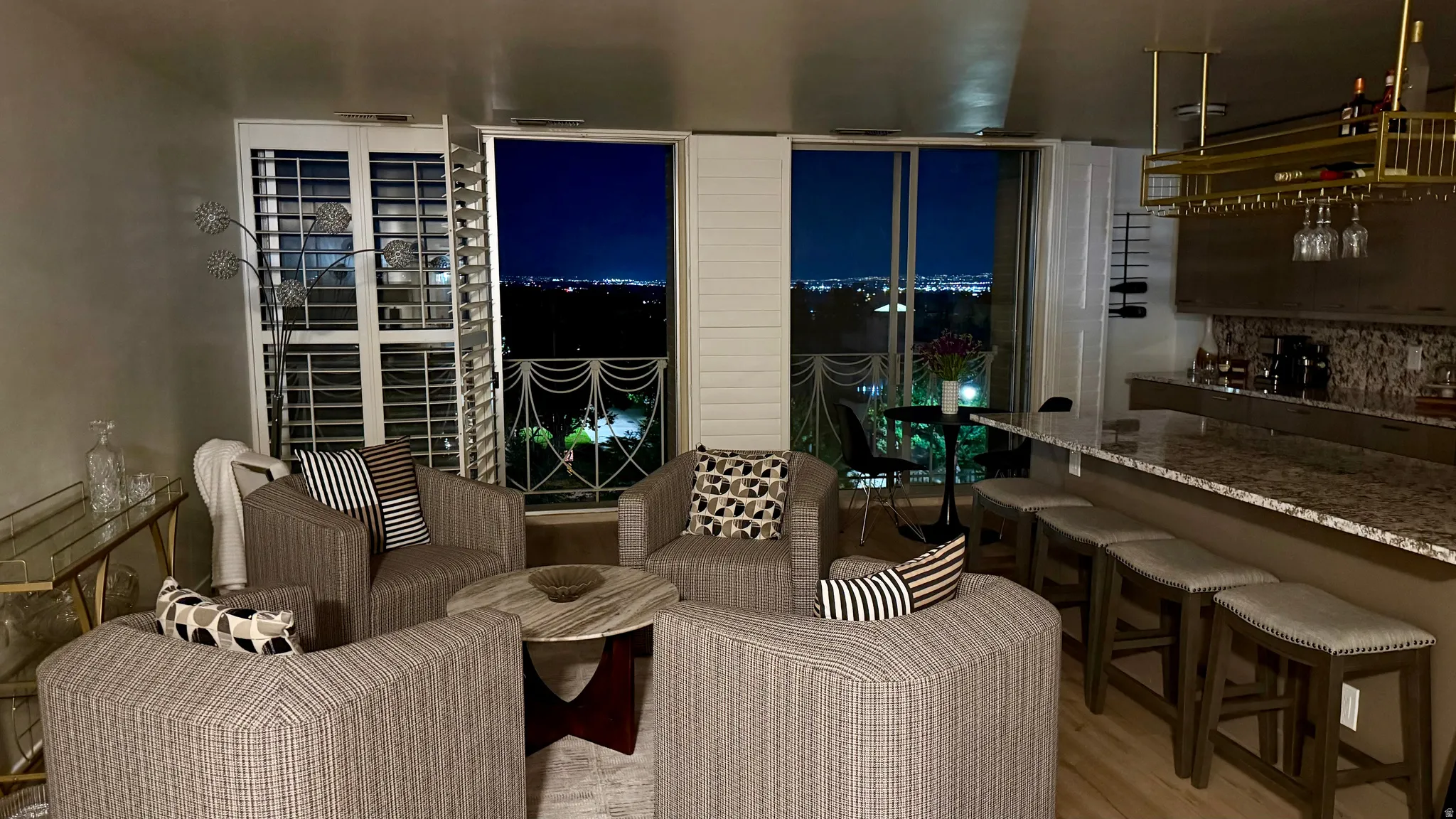 Open living area with wood-finish flooring, a built-in bar featuring a gold-finish hanging wine rack, an extended countertop with seating for four, and exterior access to a balcony through sliding glass doors