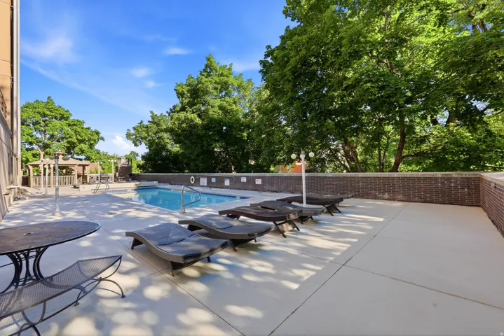 Outdoor pool area featuring a perimeter brick wall, concrete decking, and mature trees providing natural shading