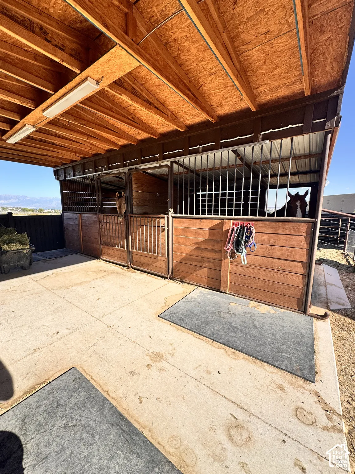 Covered stable structure featuring multiple stalls with wood-finish siding and metal bar enclosures