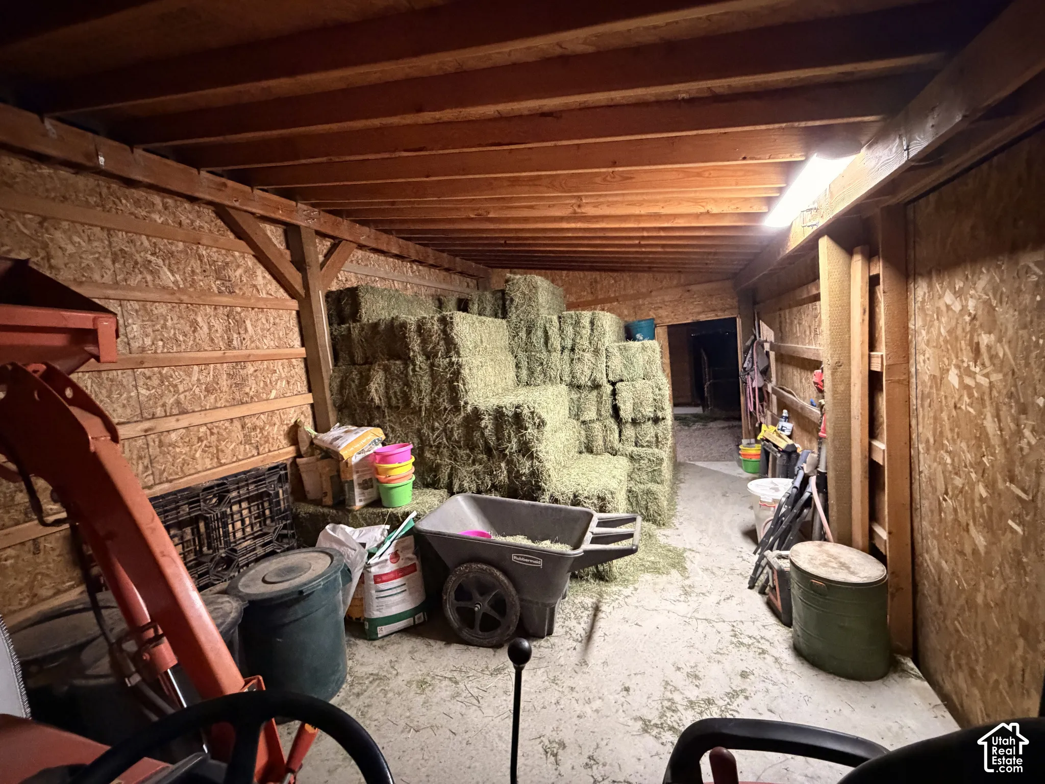 Enclosed storage structure featuring exposed timber framing, oriented strand board wall panels, concrete flooring, and linear ceiling-mounted lighting