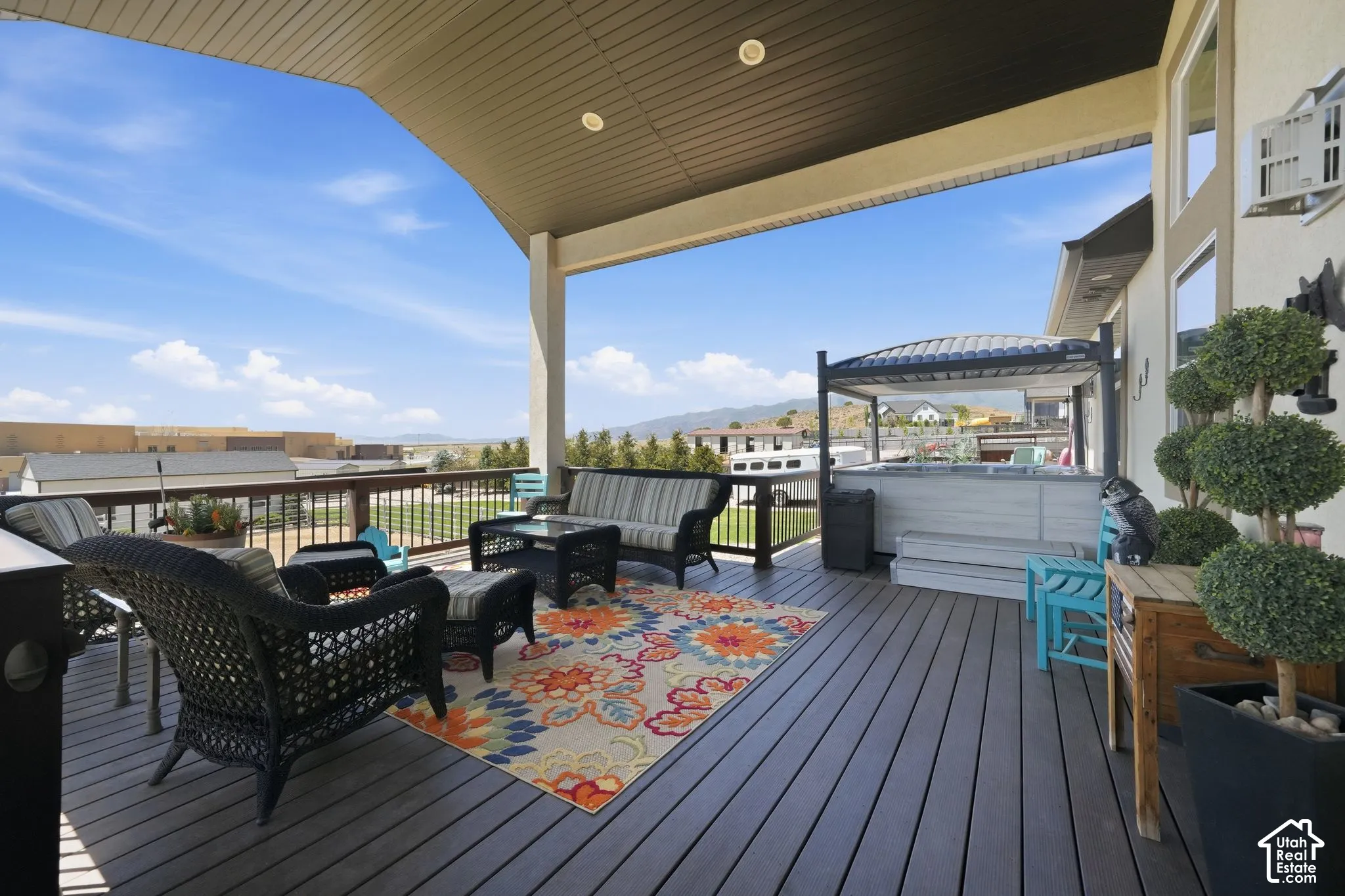 Spacious covered deck featuring composite decking, white siding, and a hot tub with an overhead pergola