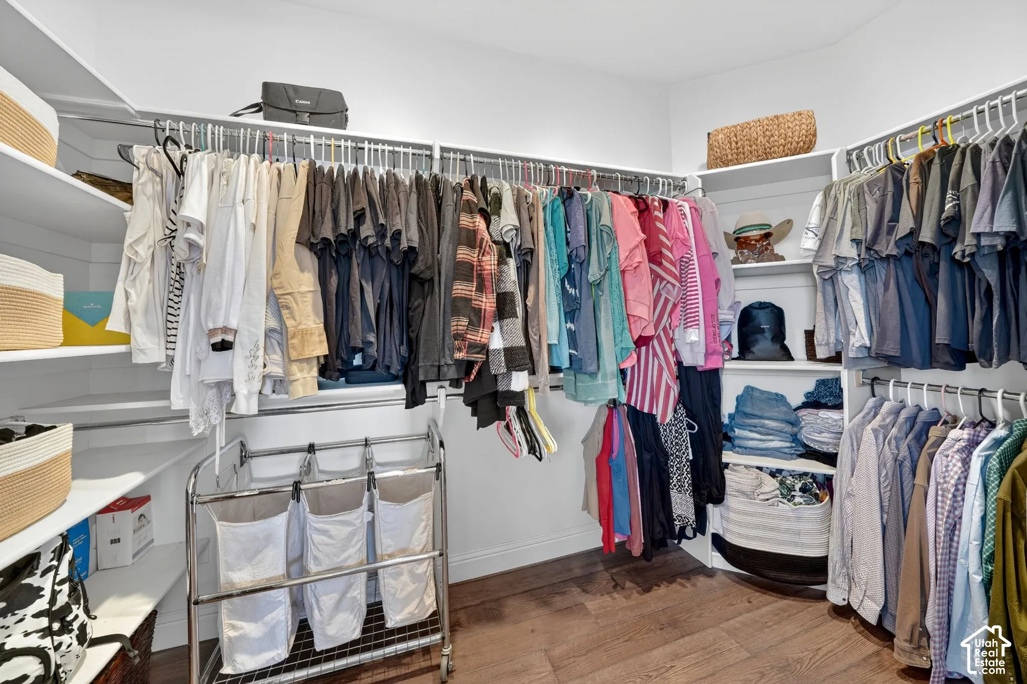 Spacious walk-in closet featuring white built-in shelving, multiple hanging rods, and wood-finish flooring