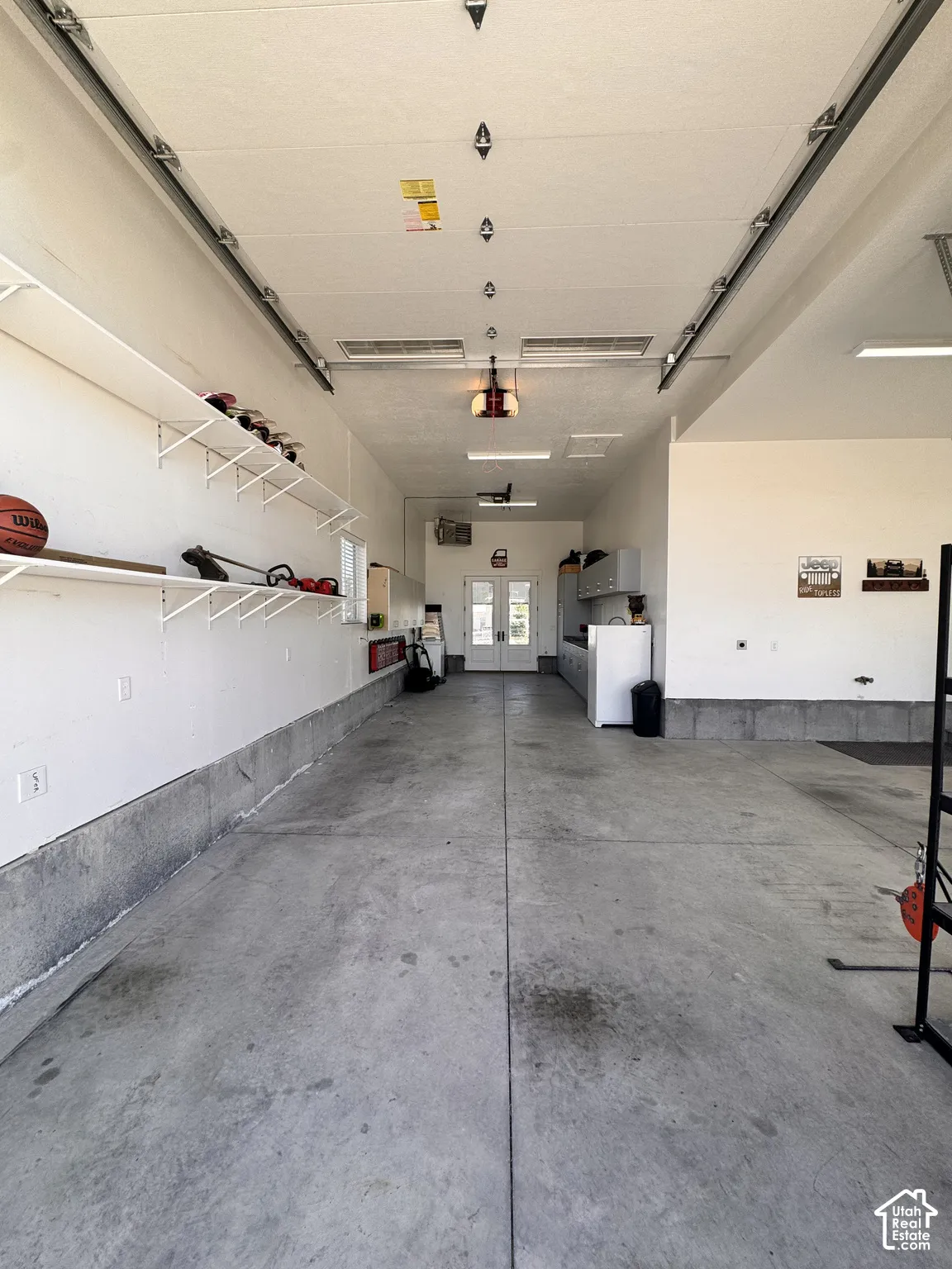 Spacious garage featuring a concrete floor, built-in shelving, overhead lighting, and white walls