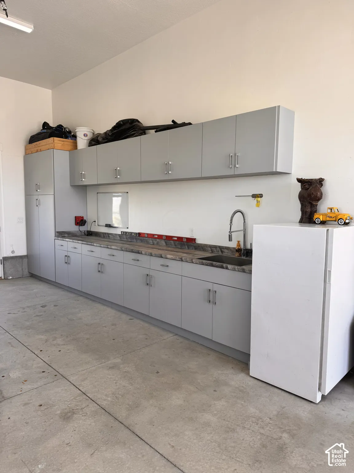Garage workspace featuring extensive light gray cabinetry, a built-in sink with a gooseneck faucet, ample counter space, and a concrete floor