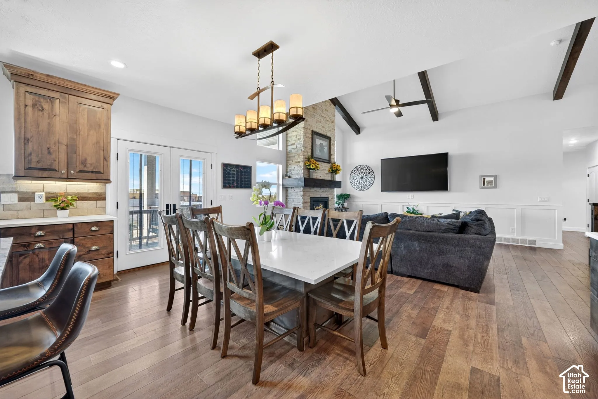 Open-concept living space featuring wood-finish flooring, a stone fireplace, and vaulted ceilings with exposed beams