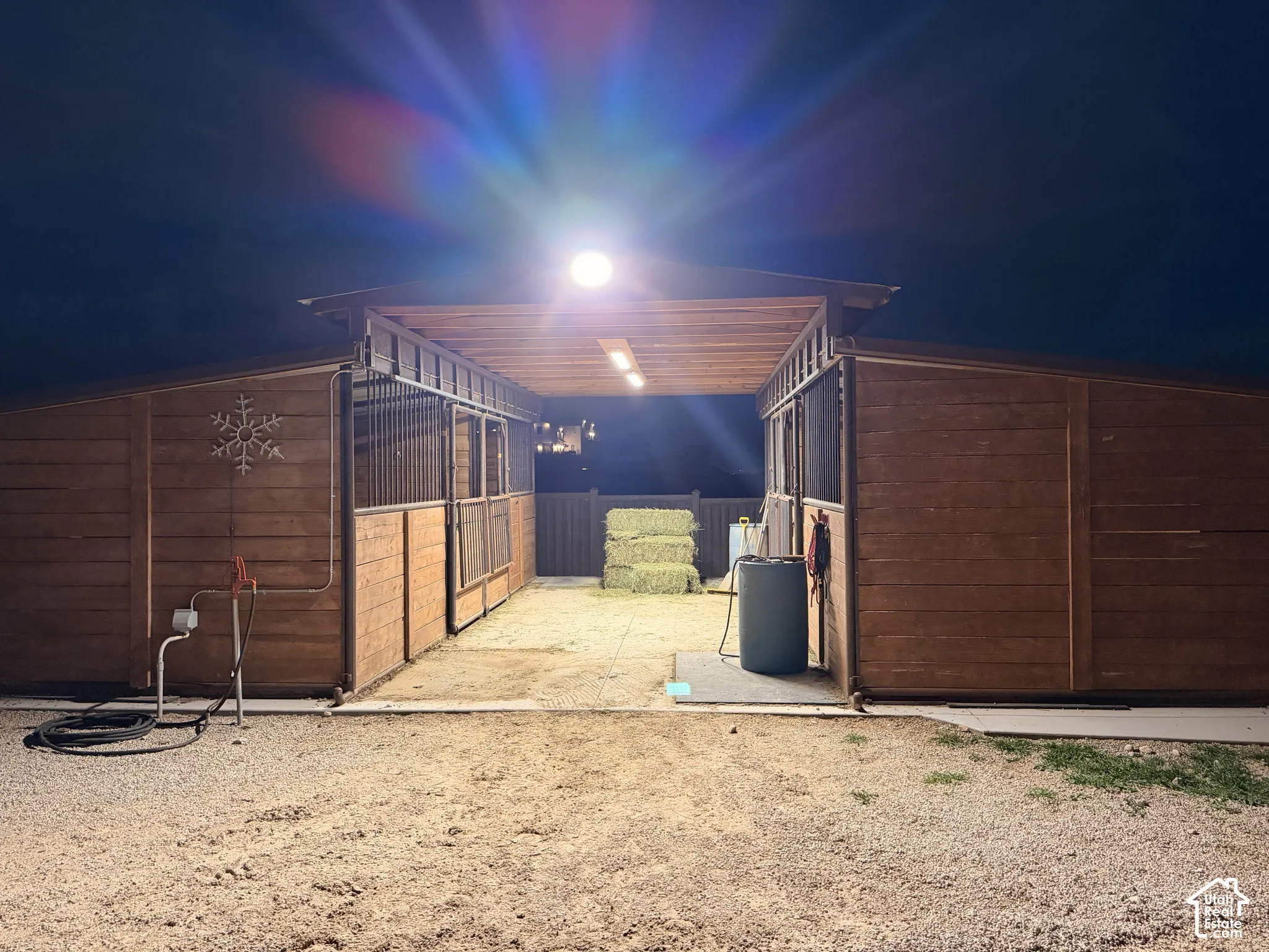 Multi-stall wood structure featuring integrated metal fencing, overhead lighting, an exposed timber-beam ceiling, and an exterior water spigot