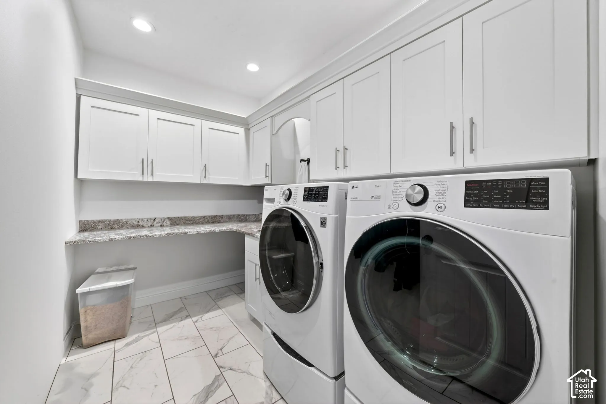 Dedicated laundry room featuring marble-look tile flooring, white shaker cabinetry, and a light-toned countertop