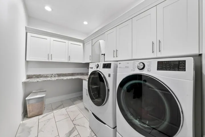 Dedicated laundry room featuring marble-look tile flooring, white shaker cabinetry, and a light-toned countertop