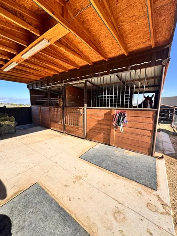 Covered stable structure featuring multiple stalls with wood-finish siding and metal bar enclosures