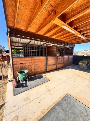 Covered equestrian facility featuring multiple wood-paneled stalls with metal grating