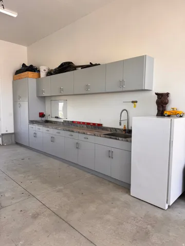 Garage workspace featuring extensive light gray cabinetry, a built-in sink with a gooseneck faucet, ample counter space, and a concrete floor