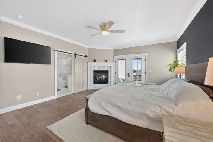 Spacious room featuring wood-finish flooring, a contemporary fireplace with a tiled surround, crown molding, and double doors opening to a balcony