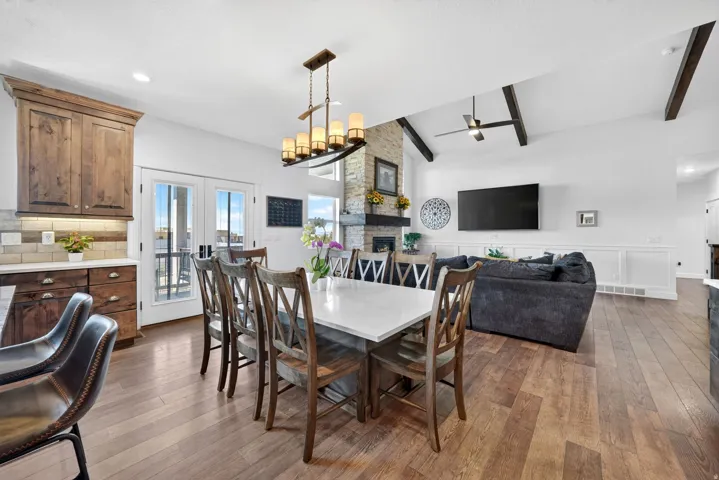Open-concept living space featuring wood-finish flooring, a stone fireplace, and vaulted ceilings with exposed beams