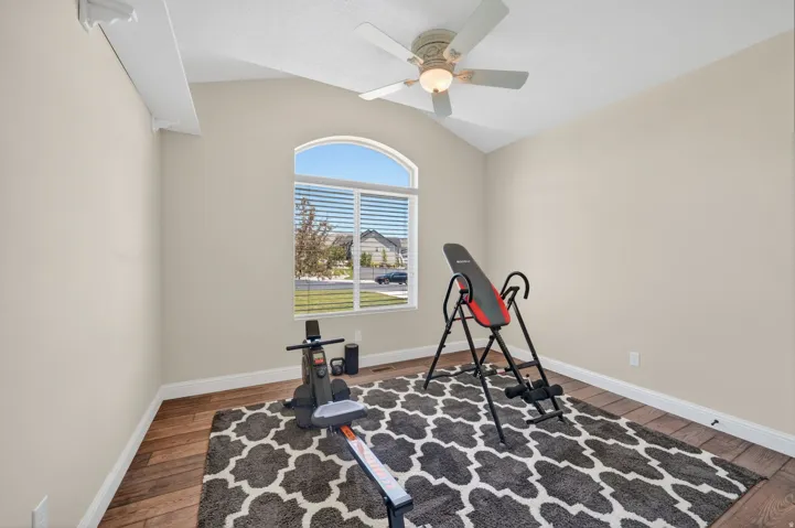 Vaulted ceiling room featuring a large arched window with horizontal blinds, wood-finish flooring, and a ceiling fan with light fixture