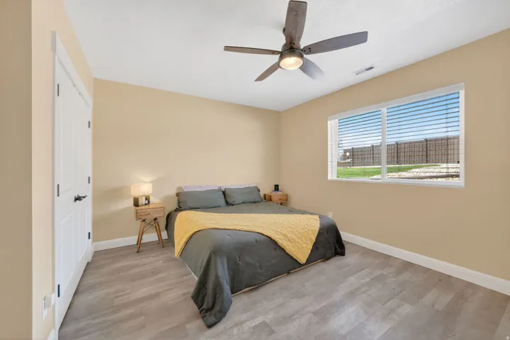 Spacious room featuring wood-finish flooring, a ceiling fan with integrated lighting, and a large window with blinds