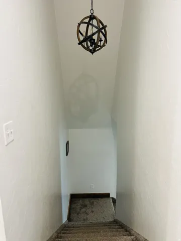 Staircase featuring a modern orb chandelier with wood and metal accents, carpeted steps, and neutral painted walls