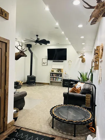 Carpeted recreation area with recessed lighting, a ceiling fan, and a wood-burning stove