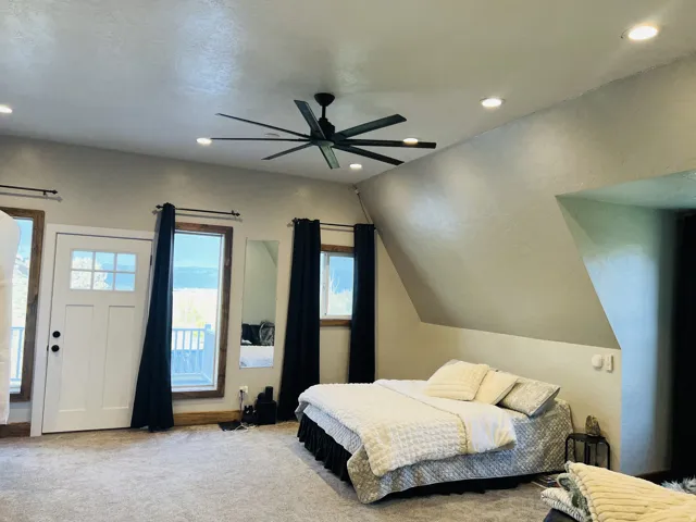 Carpeted room featuring a ceiling fan with integrated lighting, recessed ceiling lights, an exterior door with multiple glass panes, and two windows with wood-finish trim