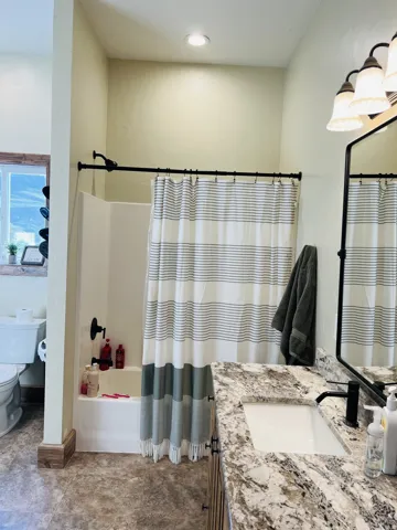 Bathroom featuring a full shower-tub combination, a vanity with a stone-finish countertop, an undermount sink, and a black-finish faucet