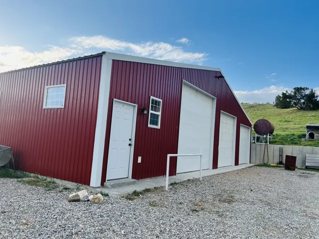Red metal-sided structure featuring multiple white garage doors and a white entry door