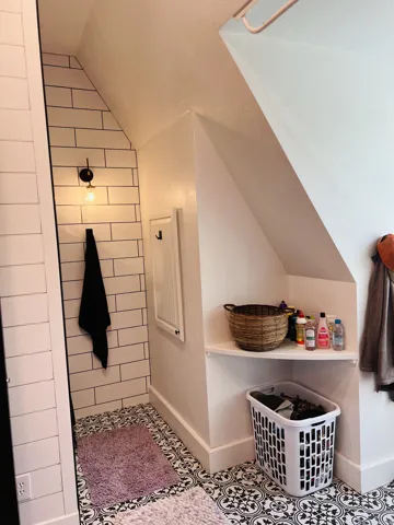 Laundry area featuring patterned floor tiles, white subway tile wall accents, a built-in corner shelf, and a wall-mounted light fixture