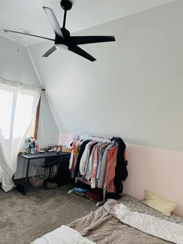 Room featuring sloped ceilings, a modern ceiling fan with integrated lighting, and neutral-toned wall finishes