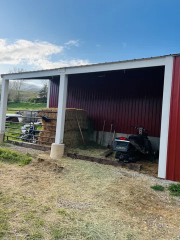 Red metal-sided open-air barn structure featuring a white support beam and a white metal roof