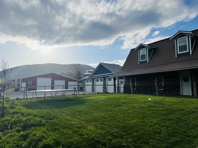 Expansive green lawn bordering a log-style residence with a brown metal roof and dormer windows