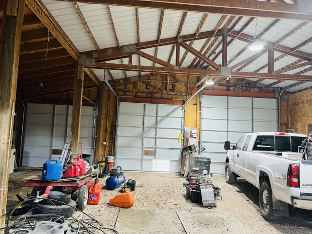 Spacious garage interior featuring multiple overhead doors, exposed wood beam construction, and overhead lighting