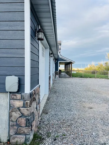 Blue horizontal siding with white trim, stone veneer foundation, multiple white garage doors with window inserts, and an extended gravel driveway