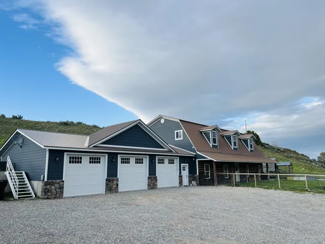Exterior featuring a multi-car garage with white paneled doors and stone accents, a durable metal roof, dormer windows, and a covered porch